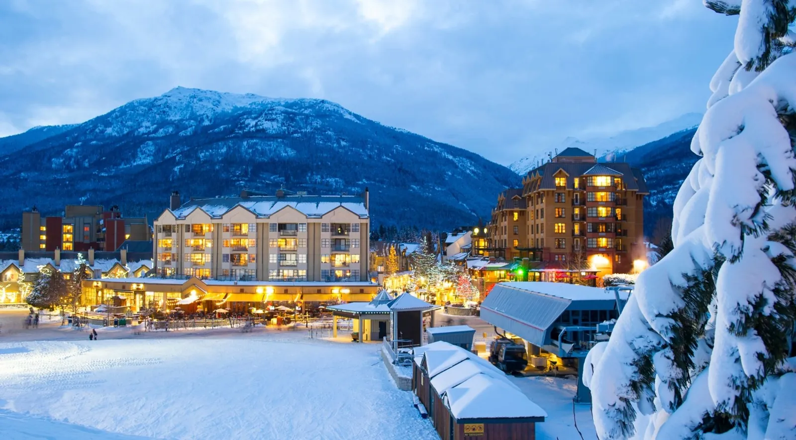 Whistler Village hotels lit up at dusk above snowy slopes and a lift station
