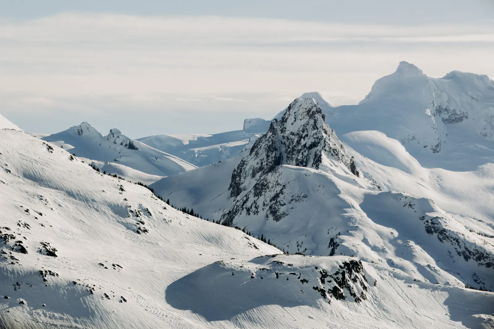 Snow-covered rocky peaks and glaciers of the Coast Mountains under a pale sky
