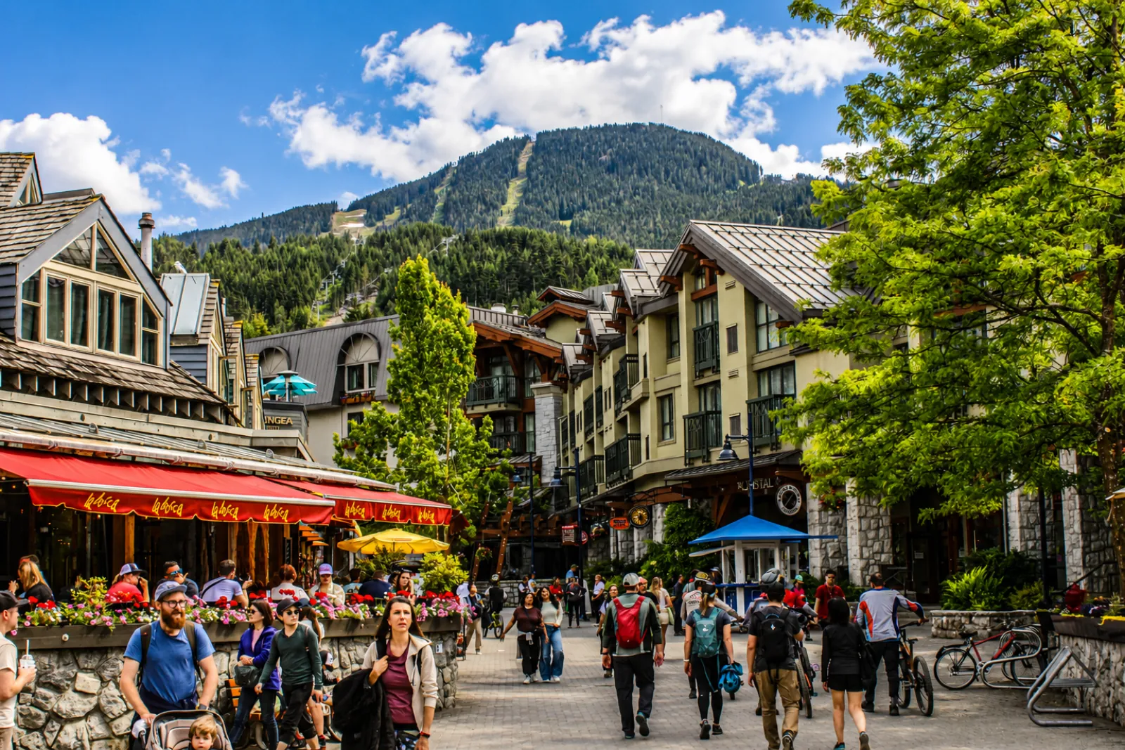 Busy Whistler Village street in summer with patios, flowers and Whistler Mountain behind
