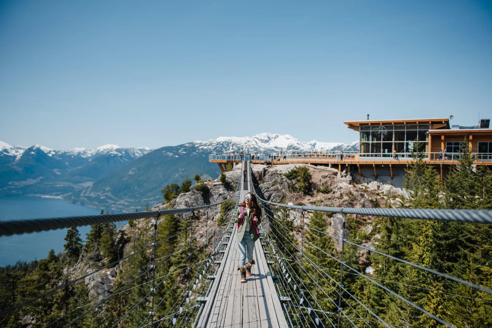 Walker crossing the Sky Pilot Suspension Bridge toward the Summit Lodge, Howe Sound behind