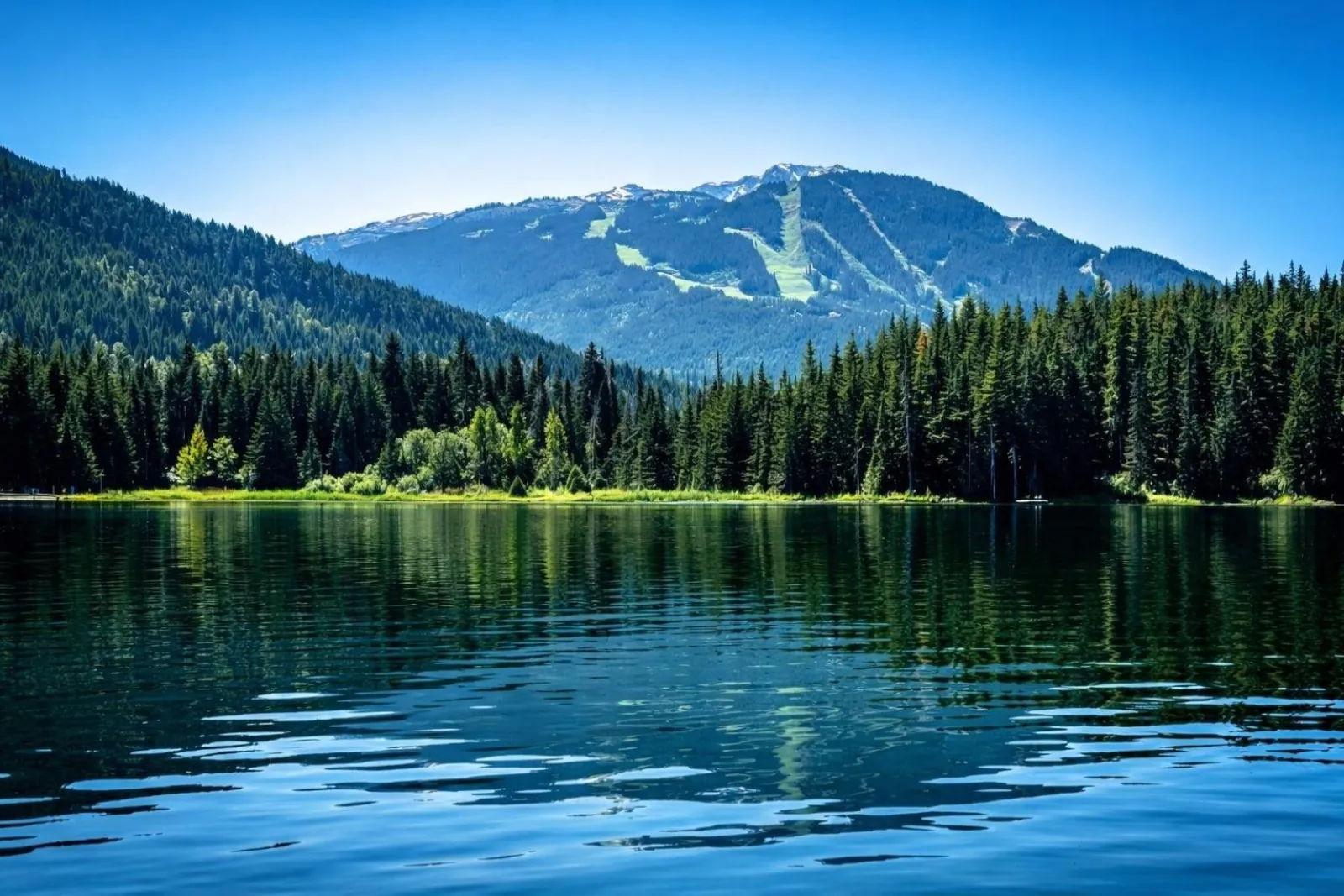 Calm lake reflecting forest below the ski runs of Whistler Mountain