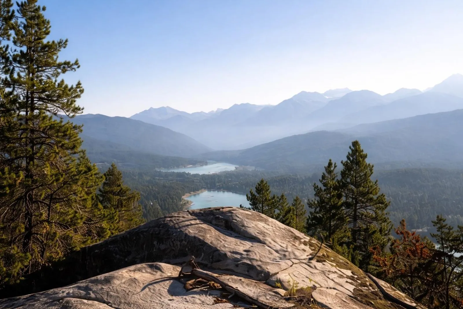 Rocky lookout over forested valleys and small lakes in hazy mountain light