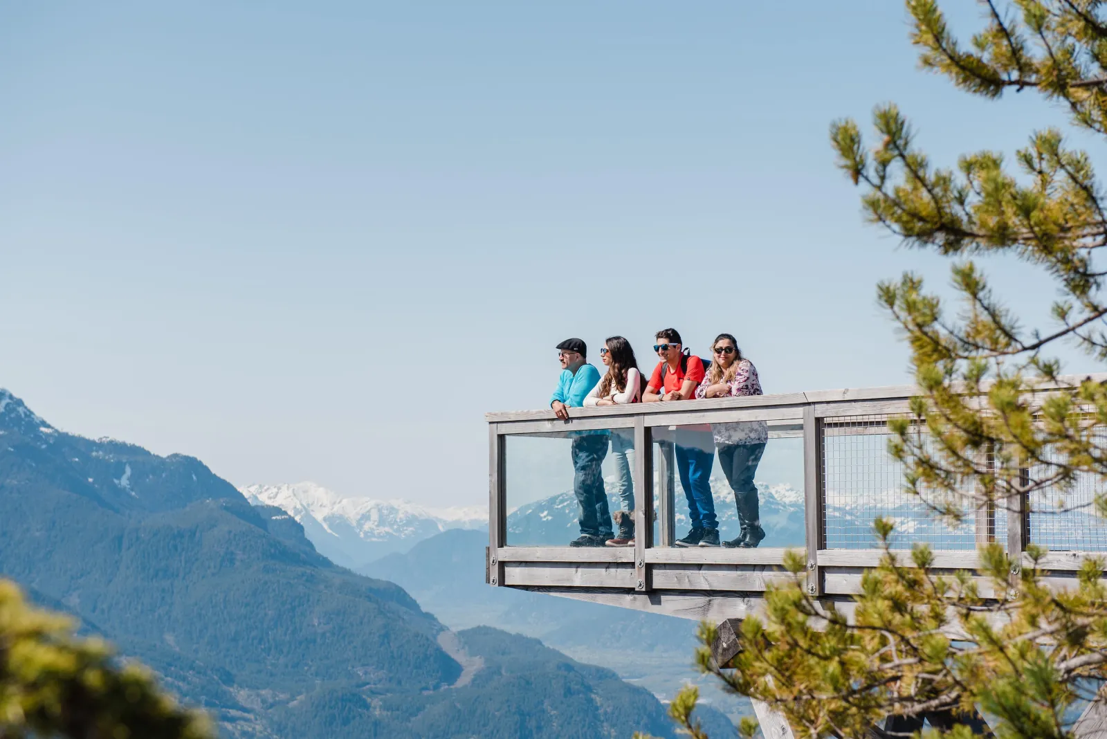 Four visitors at a glass-sided lookout over the Coast Mountains