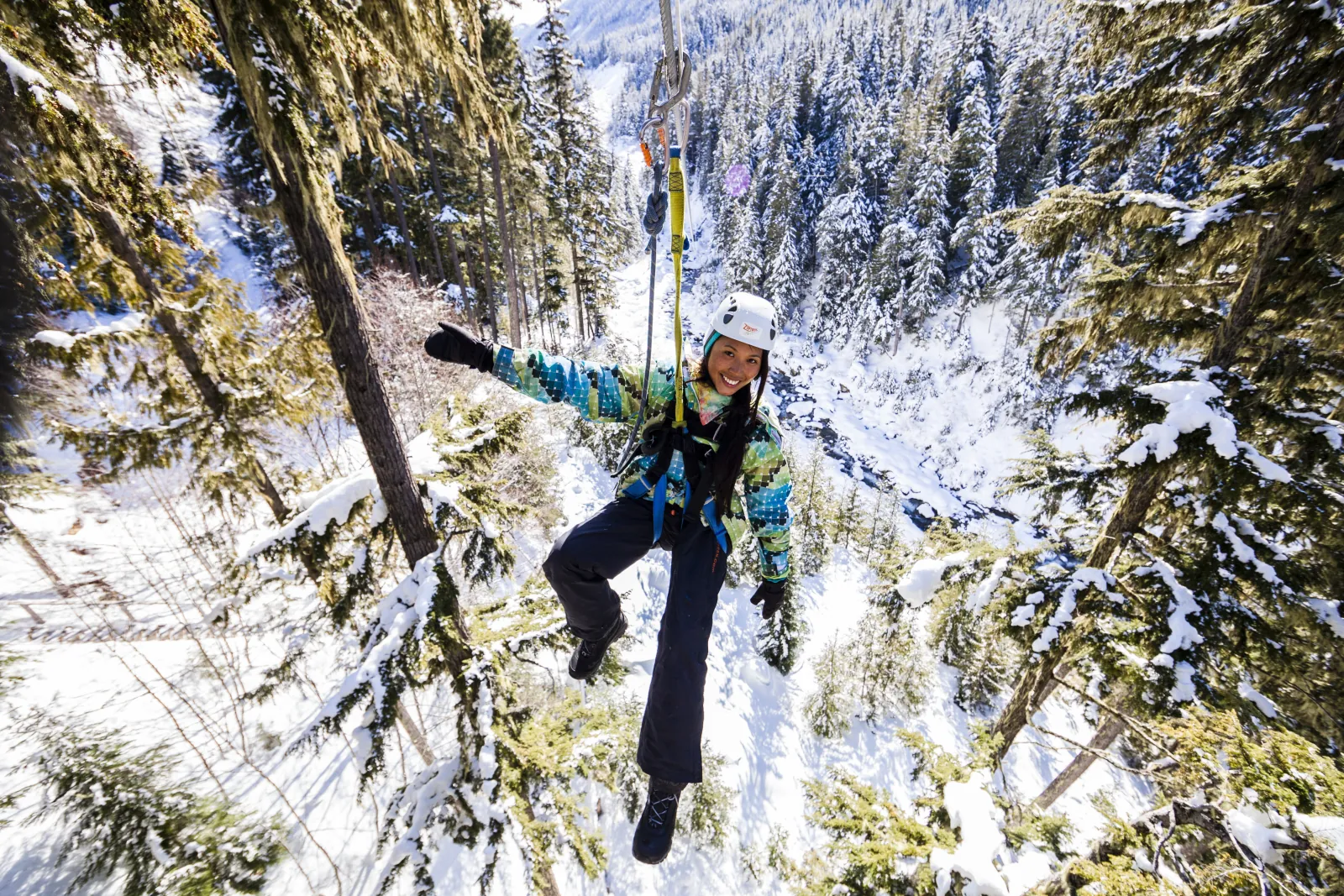 Rider on a zipline above snow-covered forest and a creek in winter