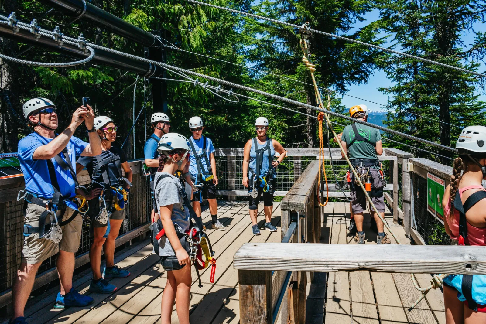 Guide briefing a group in helmets and harnesses on a wooden launch platform