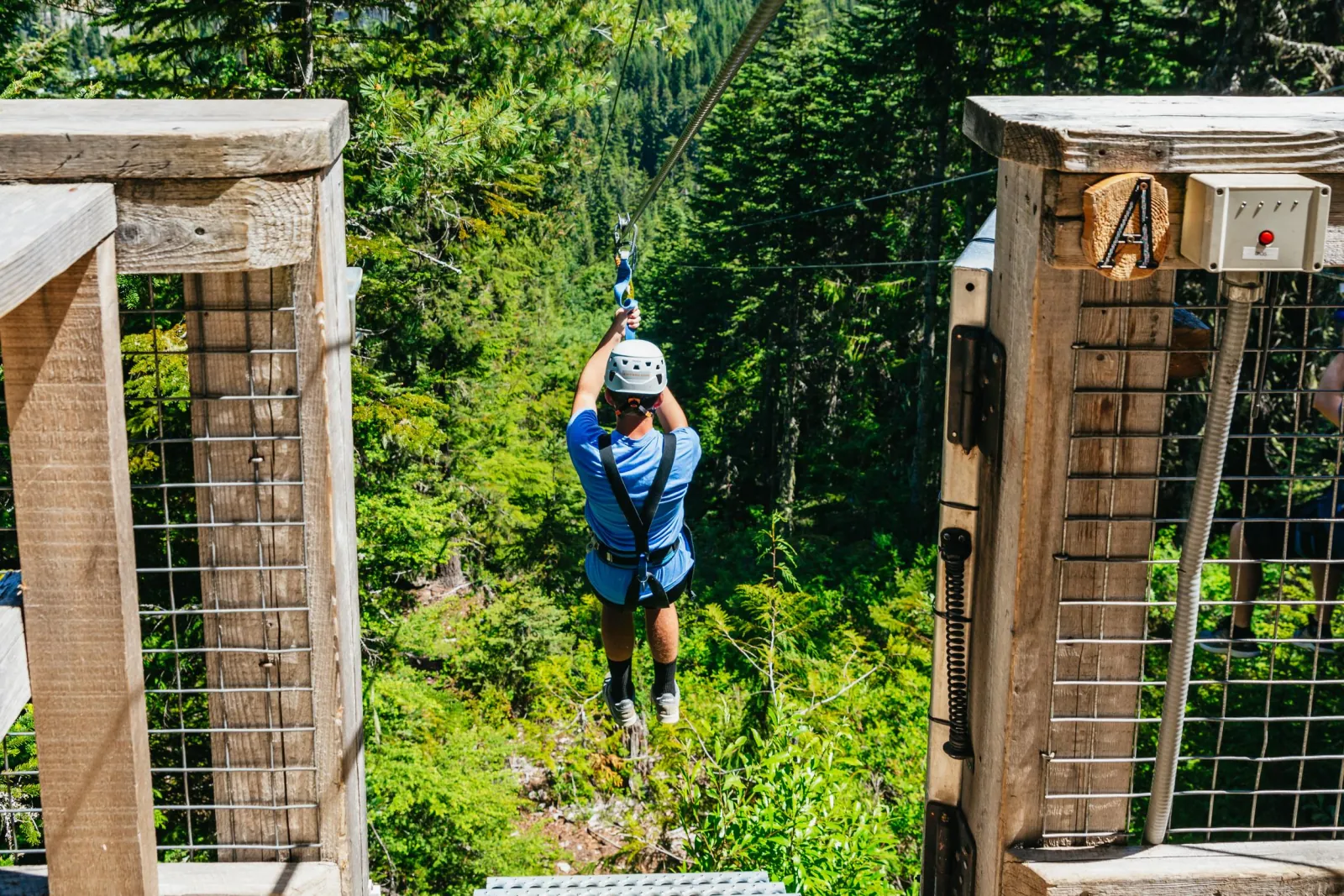 Rider launching from a wooden platform onto a zipline over a forested slope