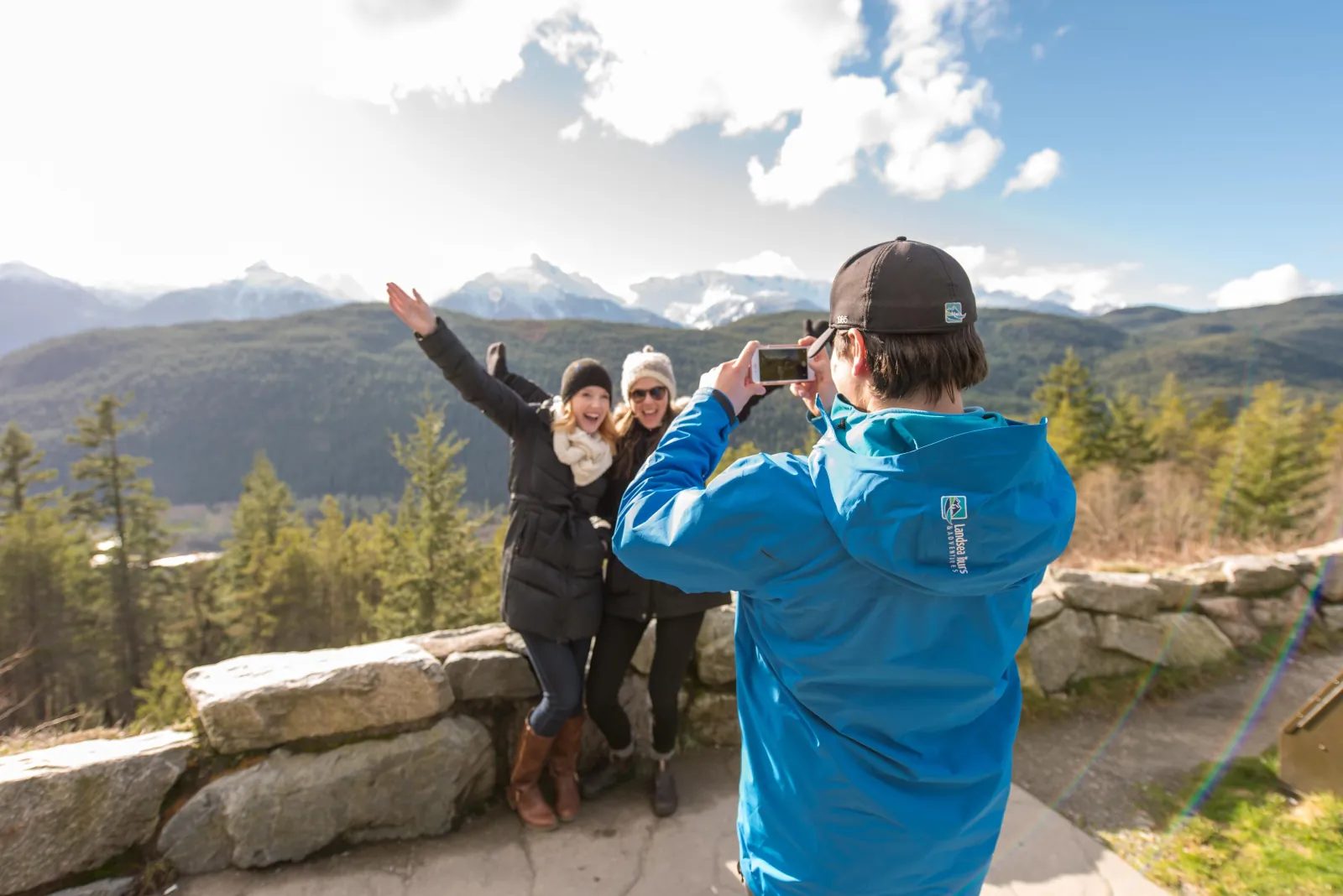 Guide photographing two guests at a stone-walled mountain viewpoint
