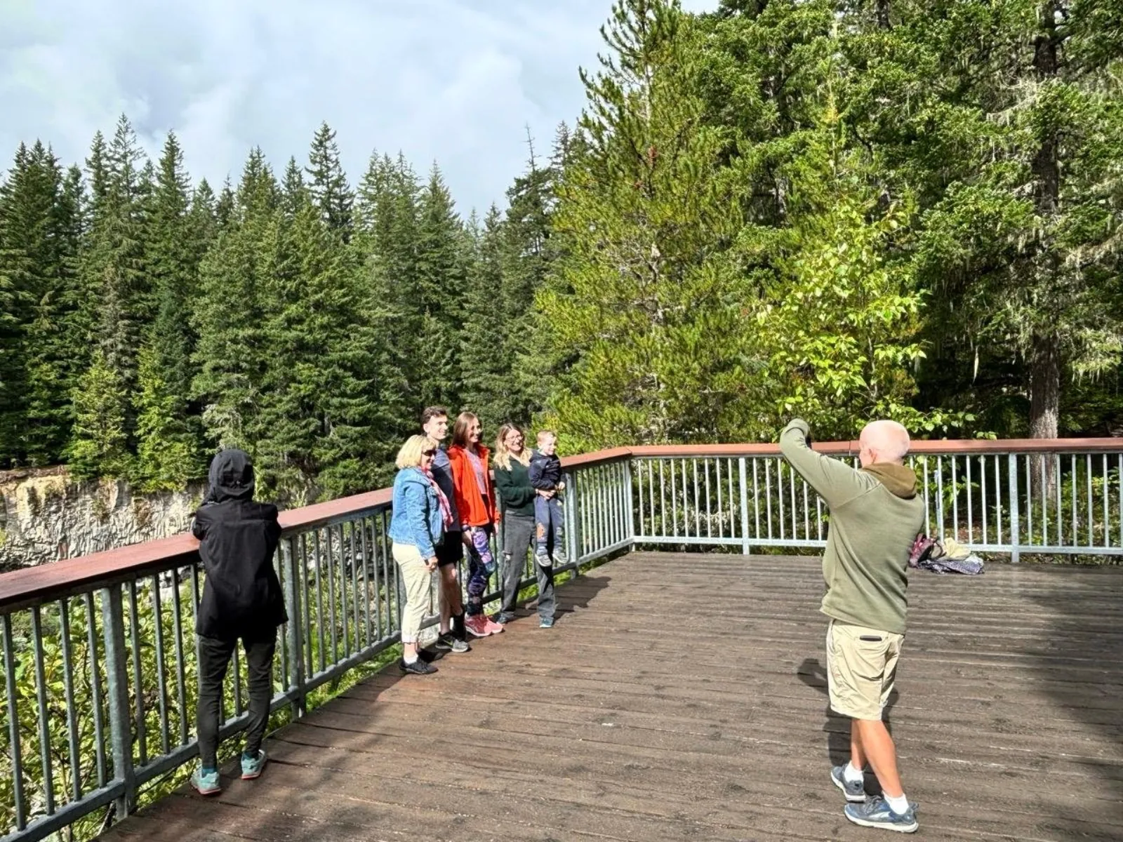 Guide photographing a family on a wooden deck above a forested canyon