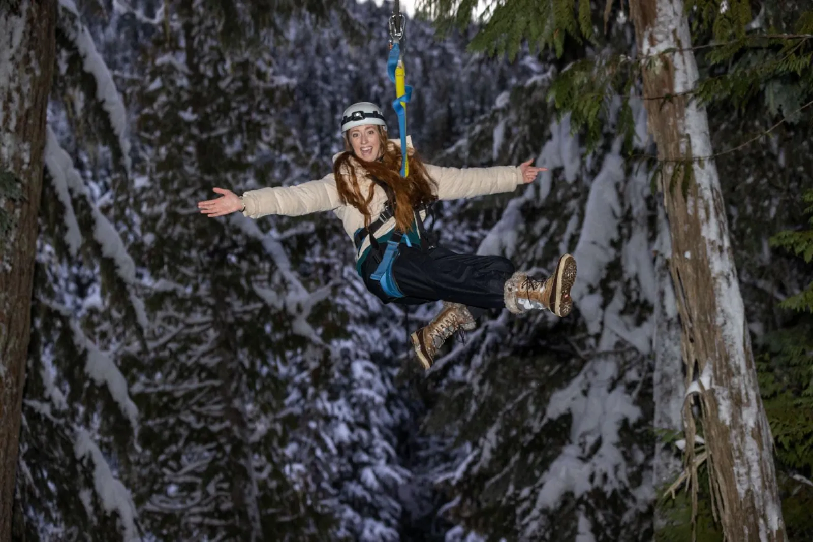 Rider with arms outstretched zipping through snow-laden forest in the evening