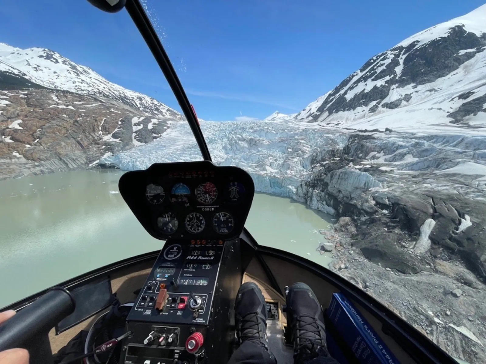 Cockpit view of a glacier snout ending in a milky meltwater lake between snowy mountains