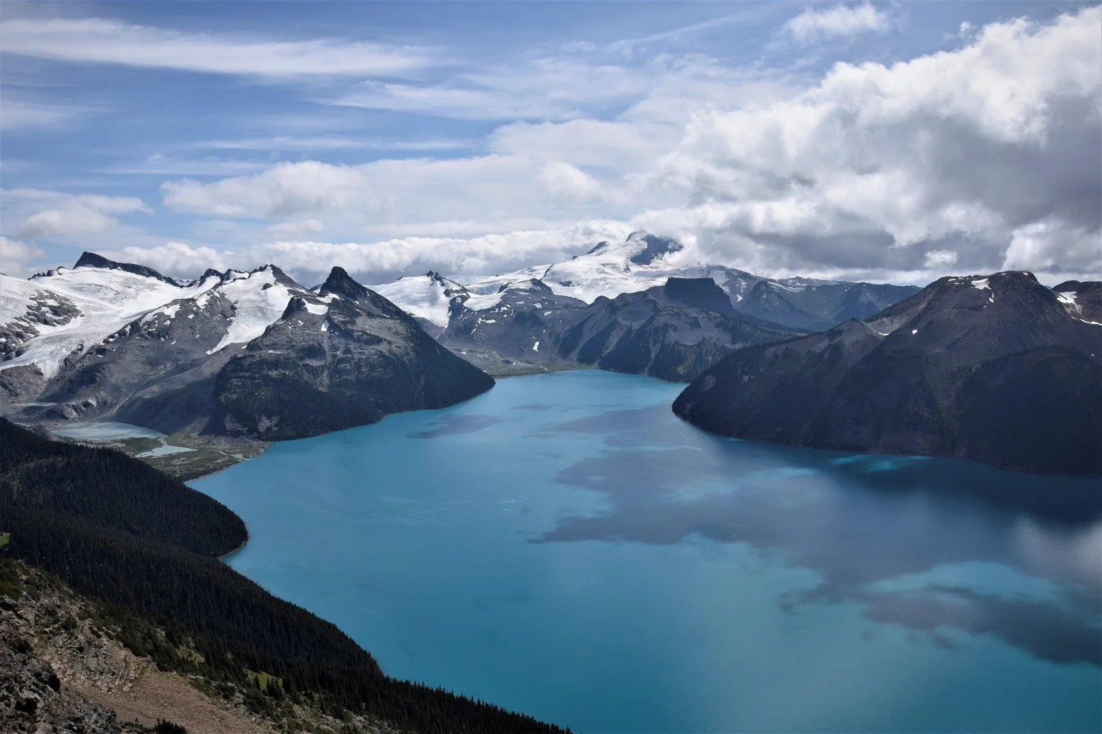 Turquoise Garibaldi Lake below glaciated peaks under a cloudy summer sky