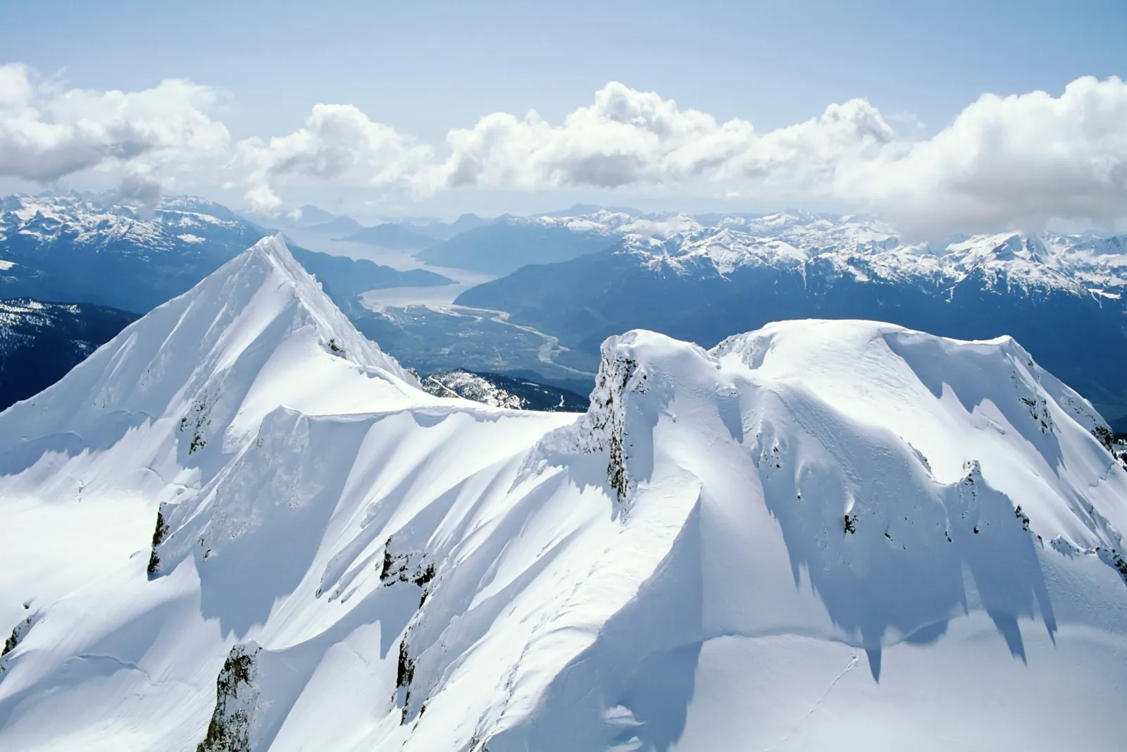 Aerial view of snow-corniced summit ridges above a river valley in the Coast Mountains