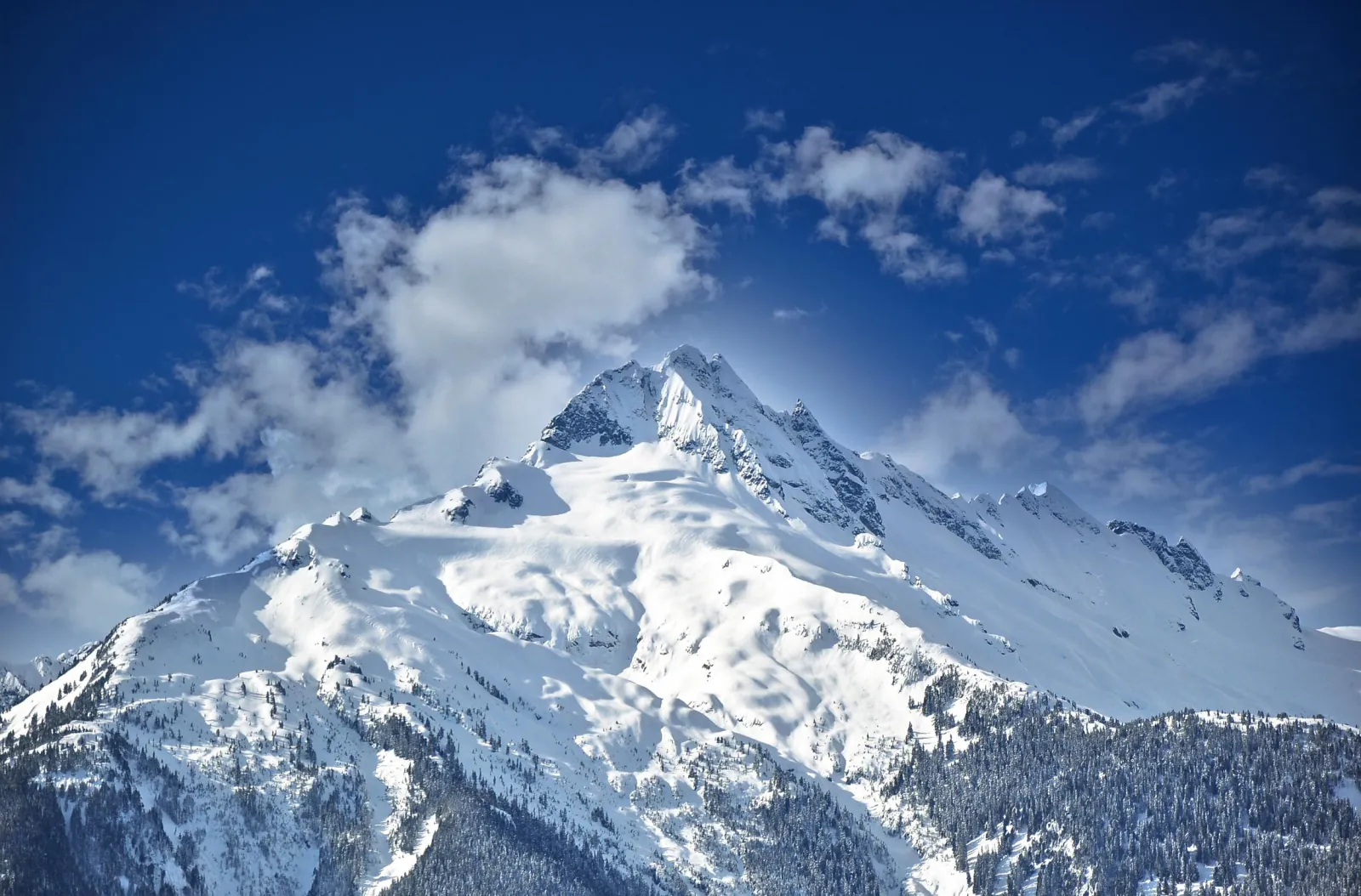 Snow-covered Coast Mountains peak against a deep blue sky with drifting cloud