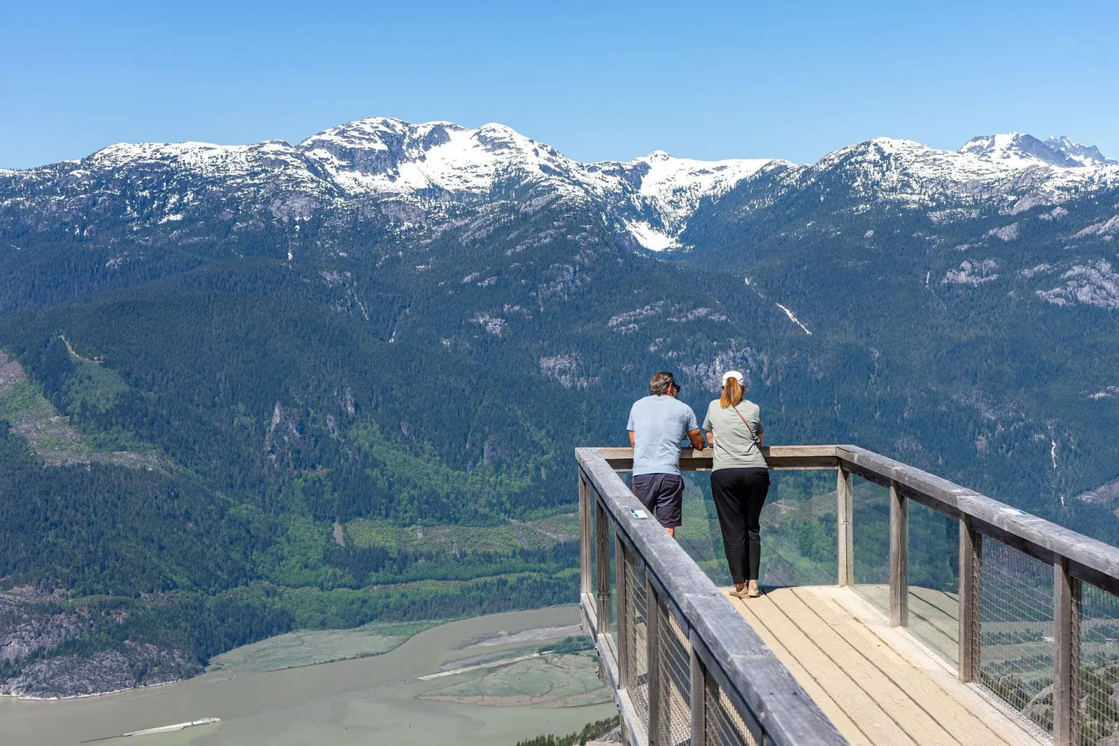 Couple at a wooden lookout facing snow-capped mountains above the Squamish valley