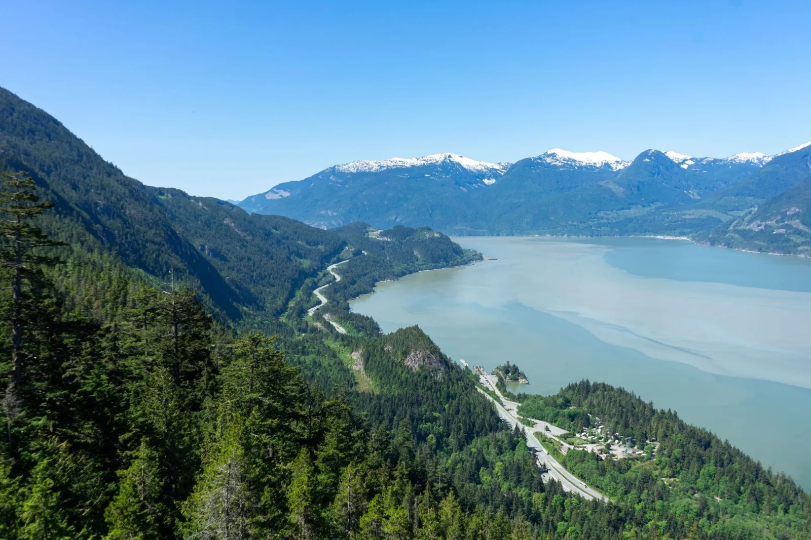Highway 99 winding along forested slopes beside Howe Sound, seen from above