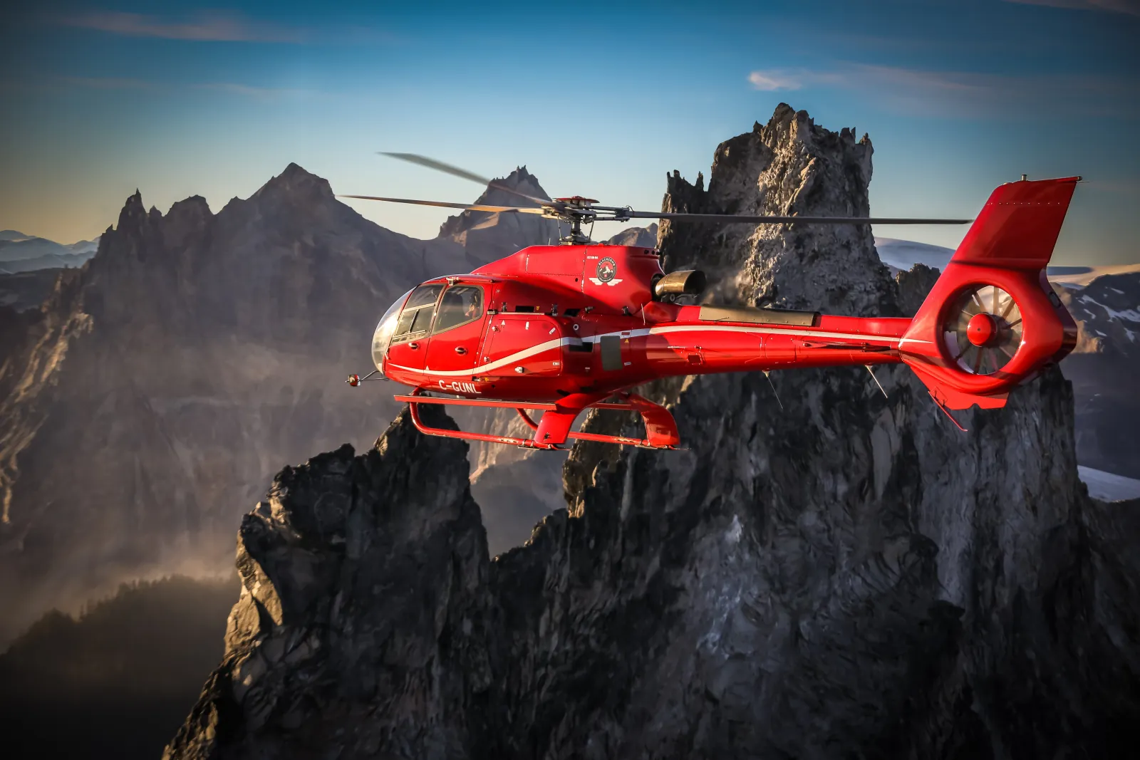 Red helicopter passing jagged granite spires in low evening light