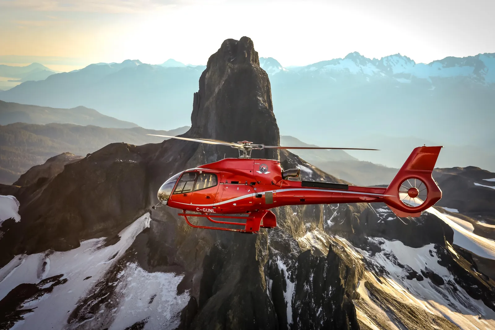 Red helicopter in front of a dark volcanic rock pinnacle with snowfields below