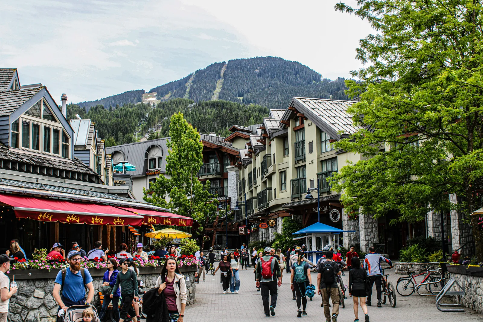 Busy Whistler Village street in summer with patios, bikes and Whistler Mountain above