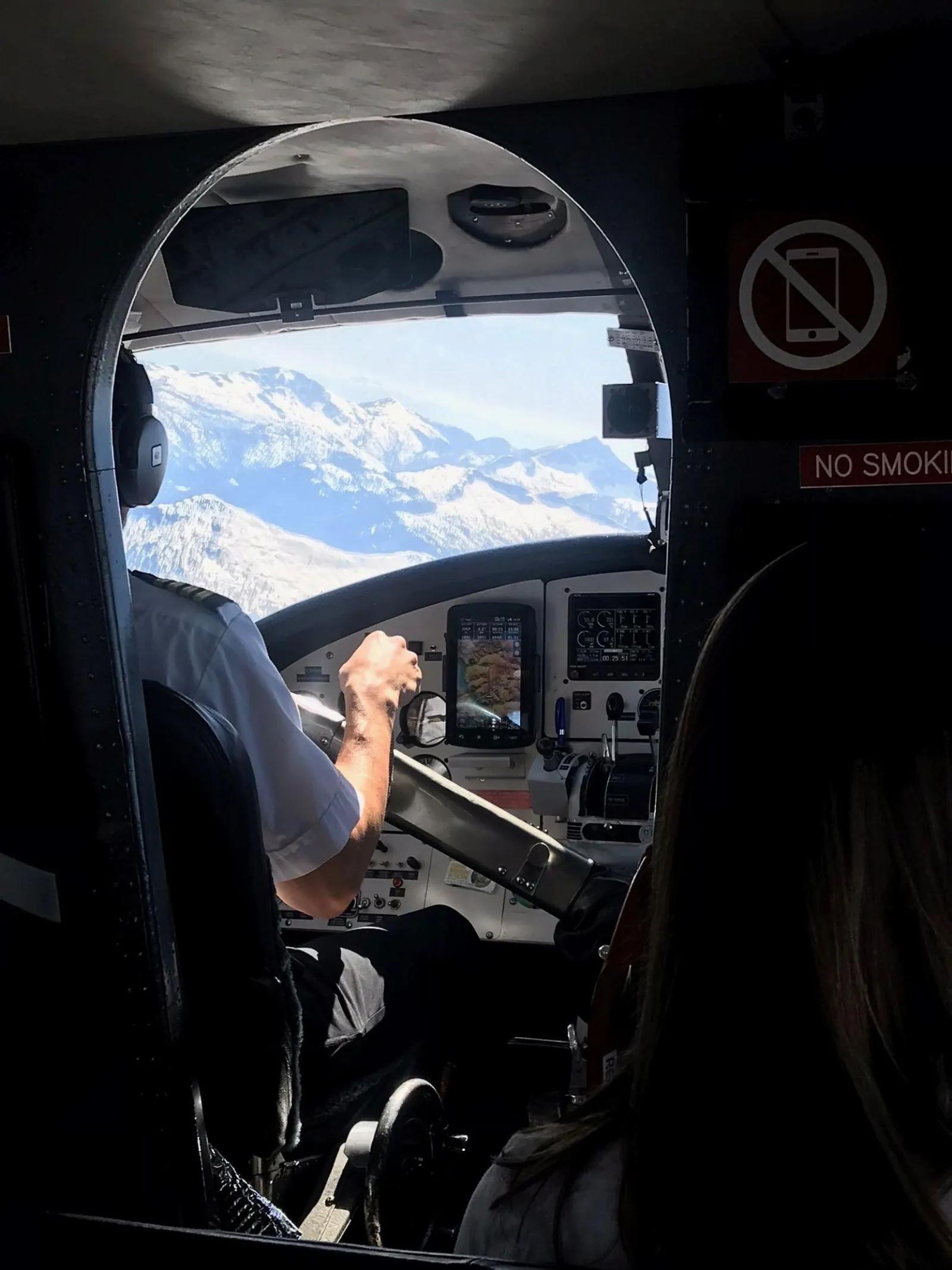 Pilot at the controls with snow-covered peaks through the seaplane windshield