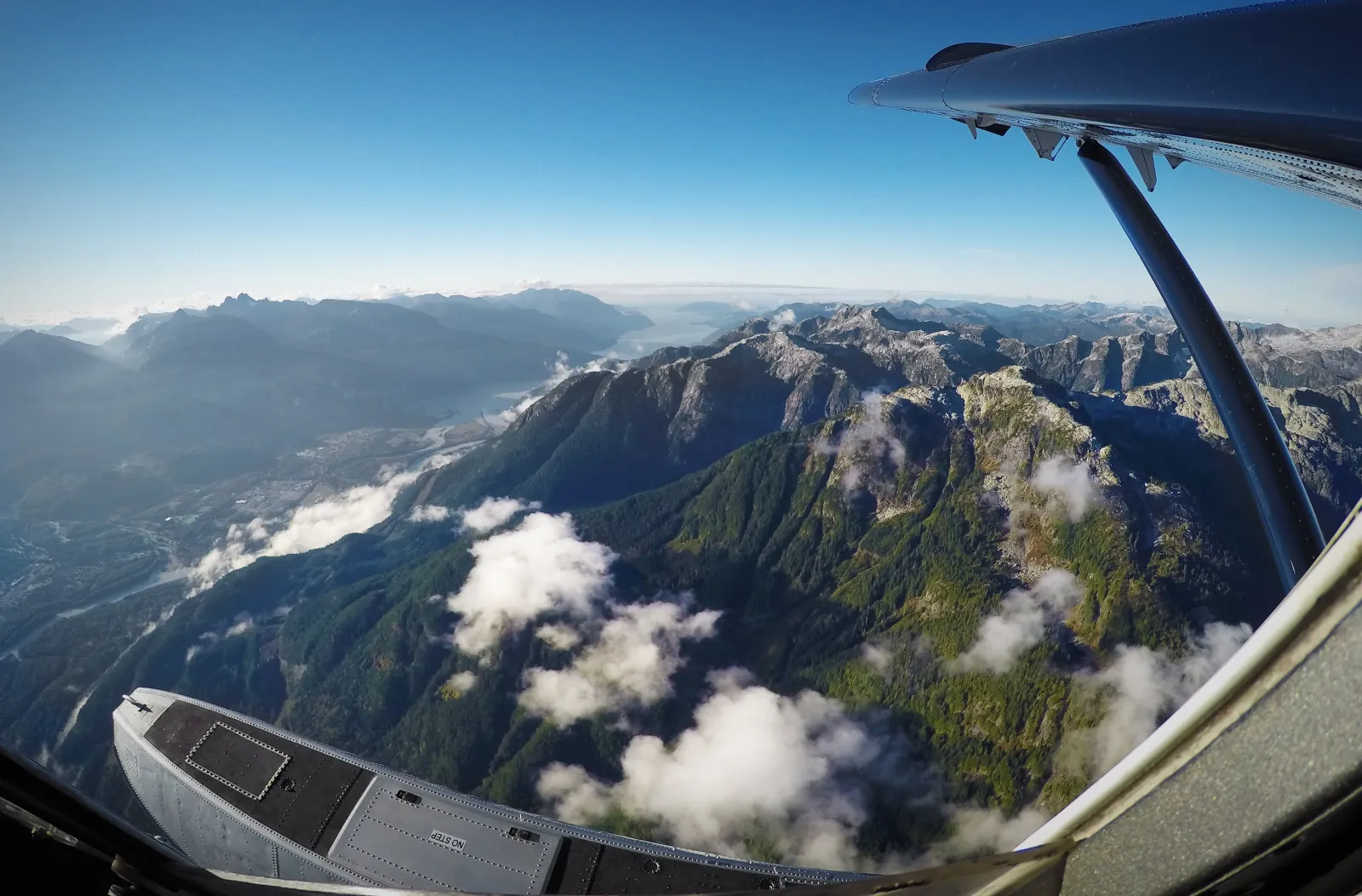 View past a seaplane float and wing strut over cloud-dotted Coast Mountains