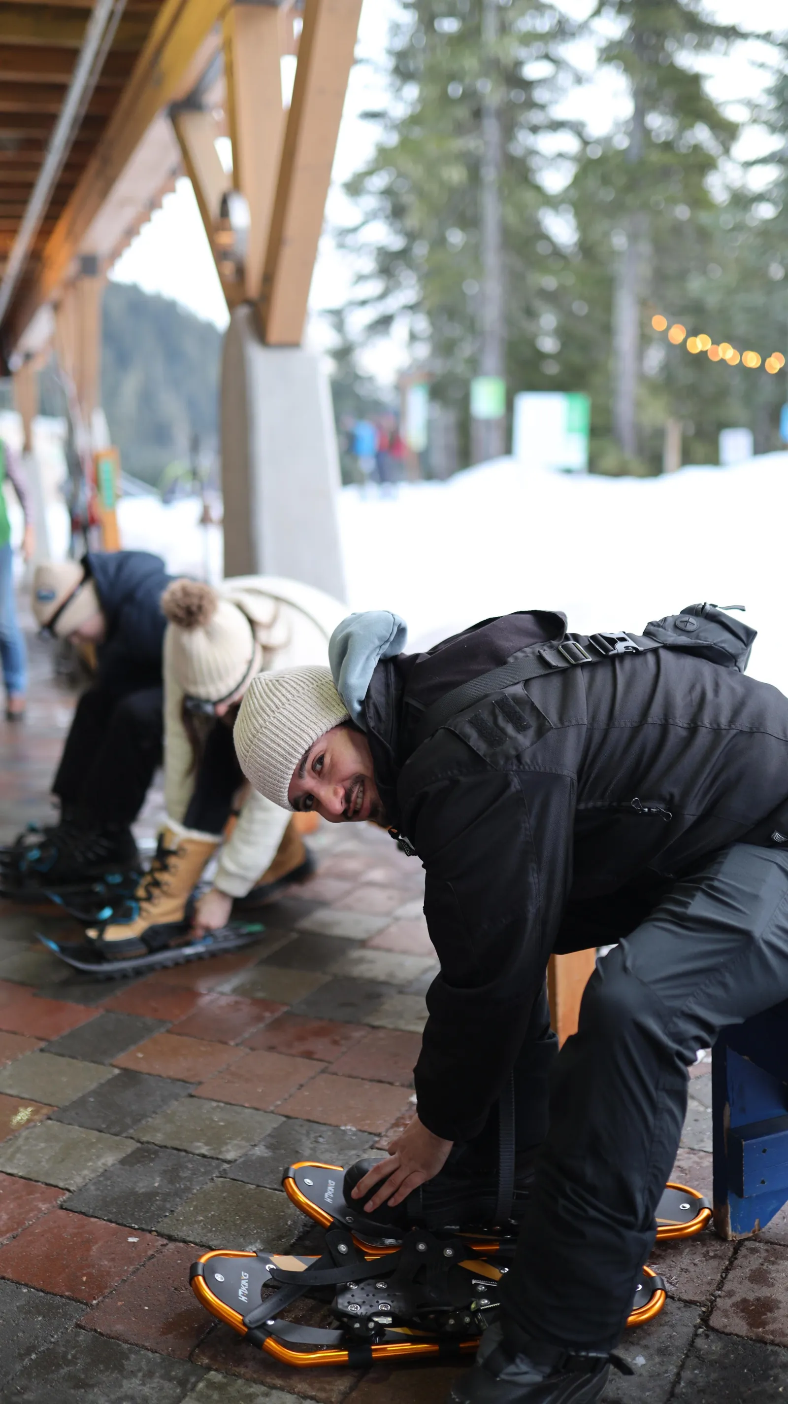 Guests strapping on snowshoes under the timber overhang of the day lodge