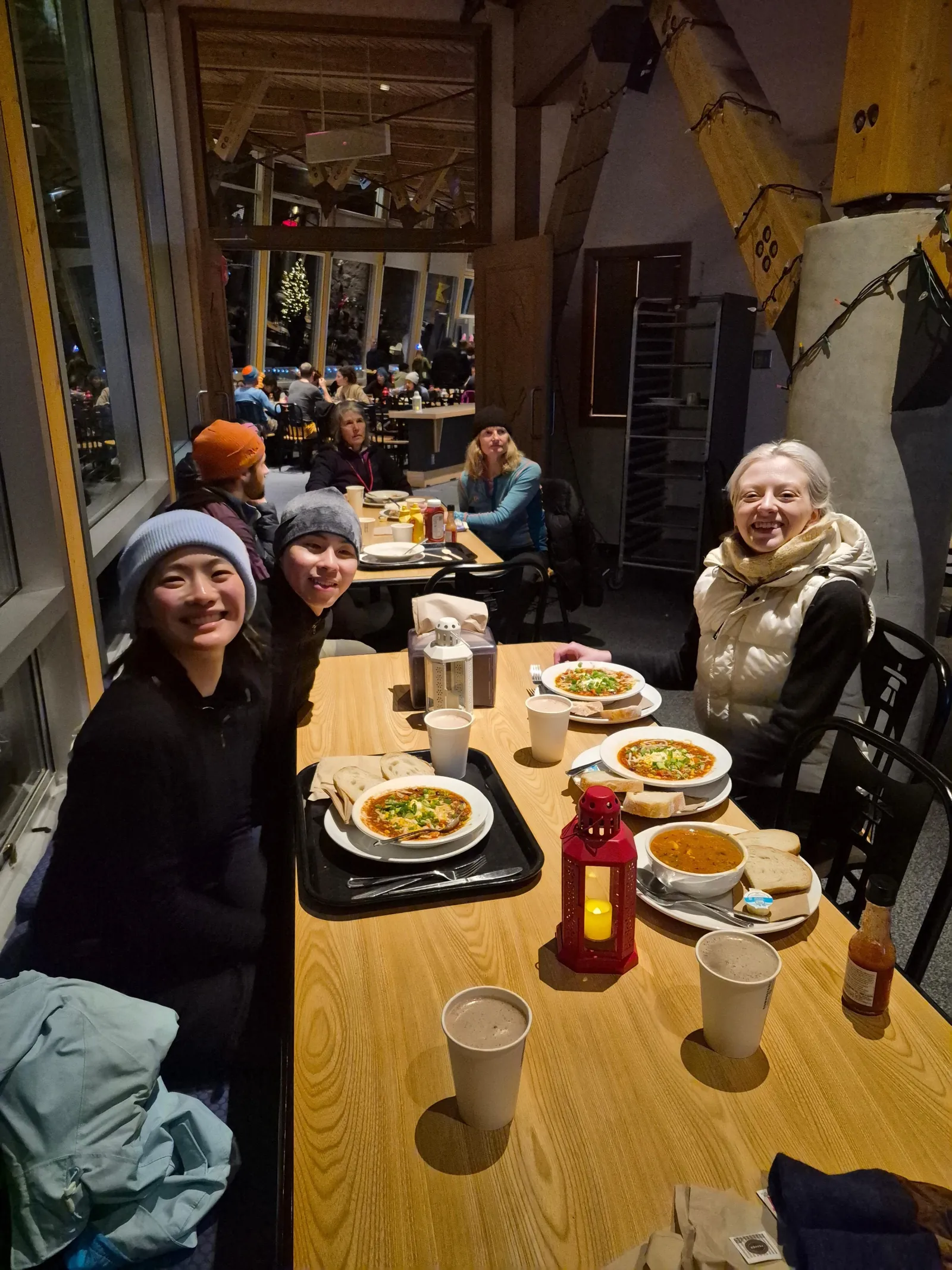 Guests at a lodge table with bowls of stew, bread and cups of hot chocolate after the trails
