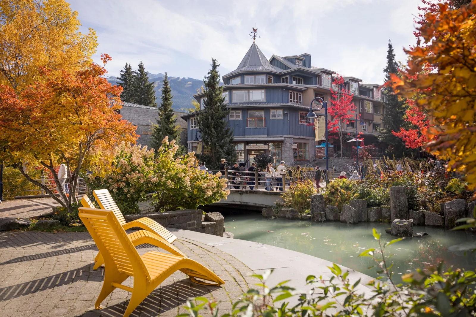 Yellow chairs by a pond in Whistler Village with autumn leaves and a turreted building