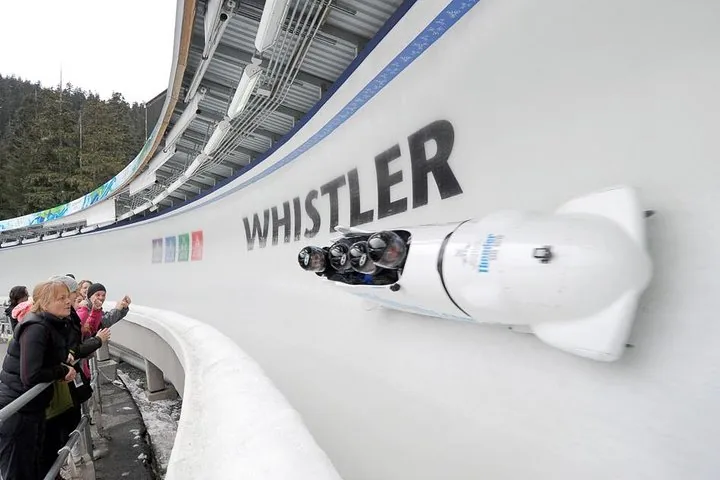 Four-person bobsled high on a curve marked WHISTLER as spectators wave from the trackside
