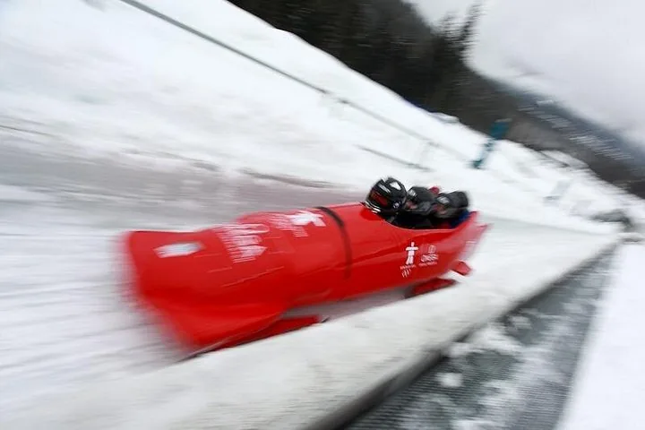 Red Whistler Sliding Centre sled with helmeted riders blurred by speed on the ice track