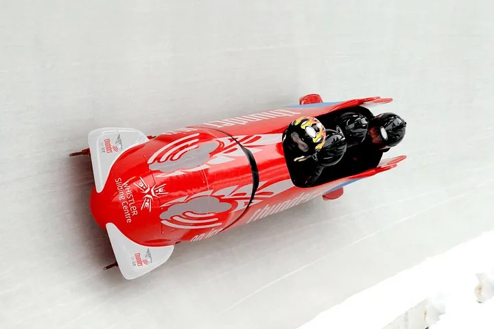 Overhead view of a red passenger bobsled with four riders sliding along the white ice