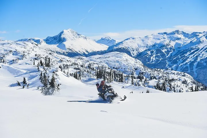 Snowmobile crossing an open alpine snowfield below a wide ring of snow-covered peaks