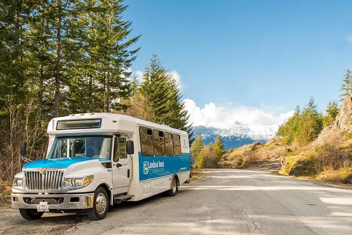 White and blue Landsea Tours minibus parked on a mountain road with snowy peaks behind