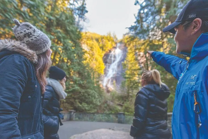 Guide in a blue jacket pointing out Shannon Falls to guests among autumn trees